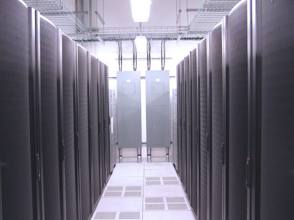 A modern data center featuring rows of black server racks aligned in a well-lit room with overhead cable trays and cooling vents visible on the floor.