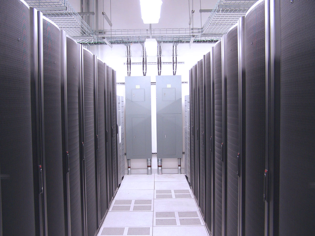 A modern data center featuring rows of black server racks aligned in a well-lit room with overhead cable trays and cooling vents visible on the floor.